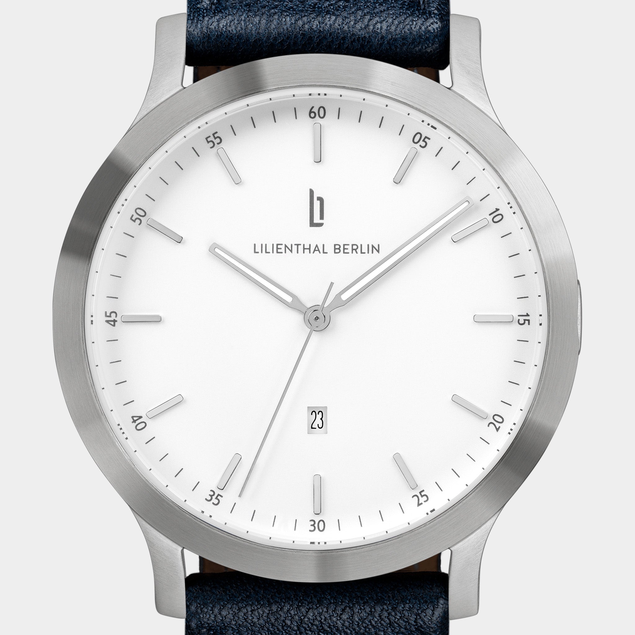 Minimalist silver watch with white dial, date window, and dark blue leather strap
