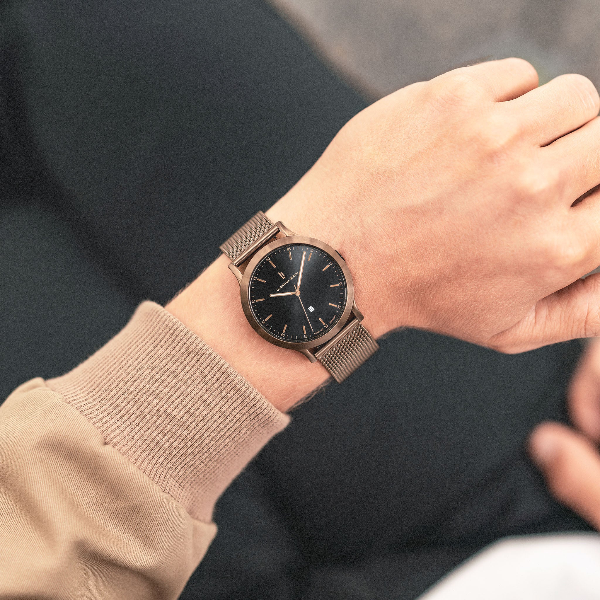 Minimalist black watch with bronze mesh strap on wrist, modern stylish design