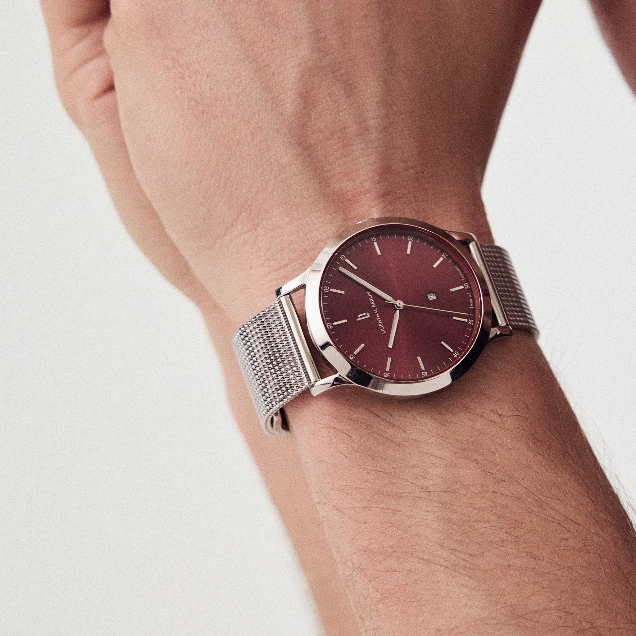 Minimalist silver mesh watch with burgundy dial on wrist, modern stylish accessory