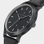 Minimalist black analog wristwatch with black leather strap and silver hour markers