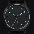 Minimalist black analog watch with luminous blue hour markers and date display