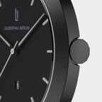 Close-up of minimalist black wristwatch with silver hour markers and geometric crown