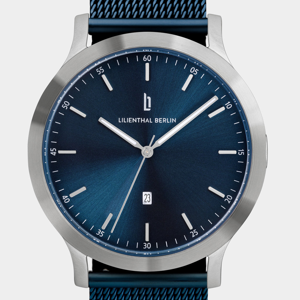 Minimalist blue dial watch with silver case, mesh strap, and date display