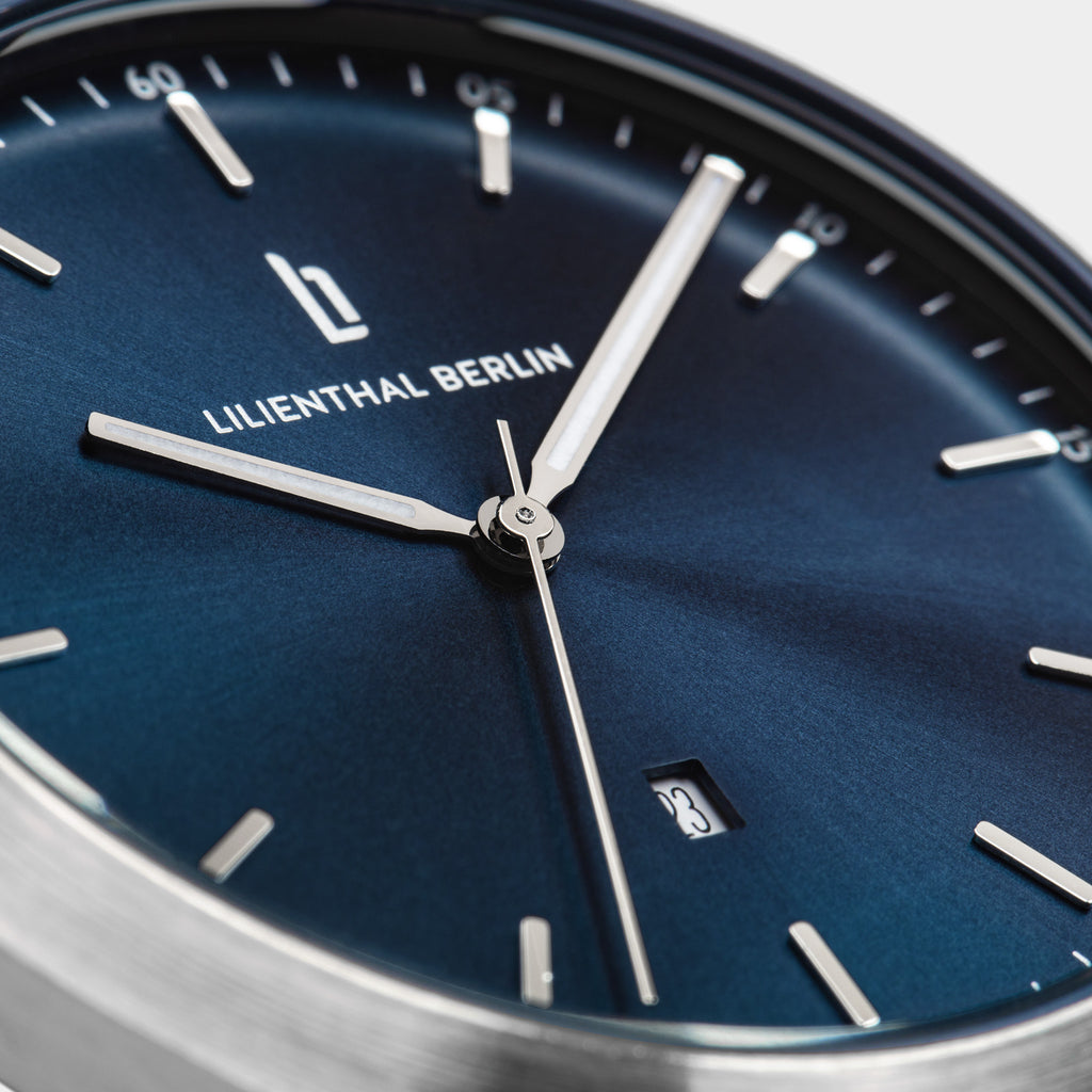 Close-up of blue dial minimalist watch with silver hands, date window, and stick markers