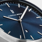 Close-up of blue dial minimalist watch with silver hands, date window, and stick markers