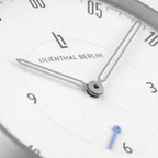 Minimalist silver watch face with slim hands, white dial, blue subdial hand, and black numerals