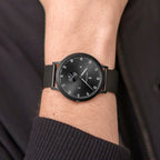 Minimalist black wristwatch with mesh strap on wrist, modern analog watch design